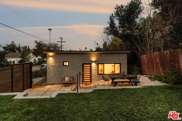 back house at dusk featuring a yard and a patio