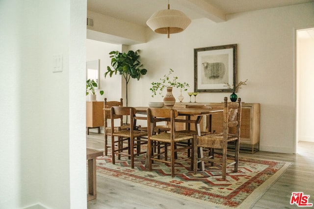 dining space with light hardwood / wood-style flooring and beamed ceiling