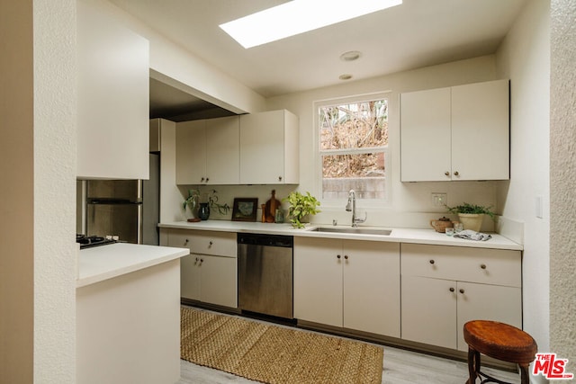 kitchen with white cabinets, appliances with stainless steel finishes, a skylight, sink, and light hardwood / wood-style flooring