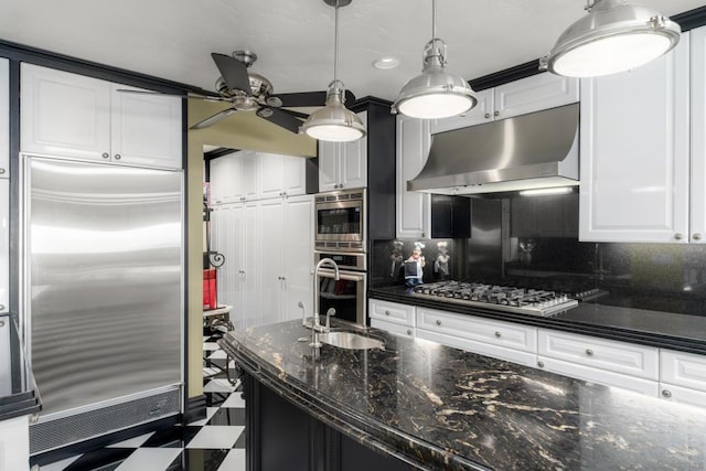 kitchen featuring hanging light fixtures, backsplash, white cabinetry, dark stone countertops, and built in appliances