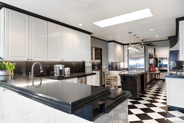 kitchen with white cabinets, decorative light fixtures, a skylight, sink, and backsplash