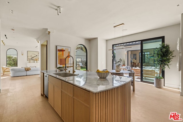 kitchen featuring dishwasher, sink, light stone countertops, a center island with sink, and light wood-type flooring