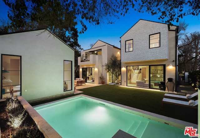 back house at dusk with a lawn, a patio, and a balcony