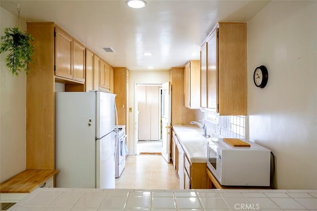 kitchen with white appliances, light brown cabinetry, and tile counters