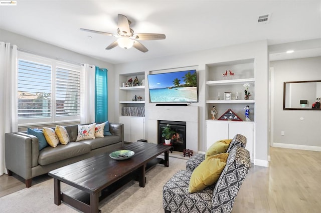 living room featuring built in features, light hardwood / wood-style floors, and ceiling fan