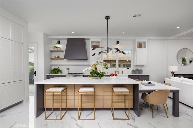 kitchen featuring decorative light fixtures, wall chimney range hood, stove, sink, and white cabinets