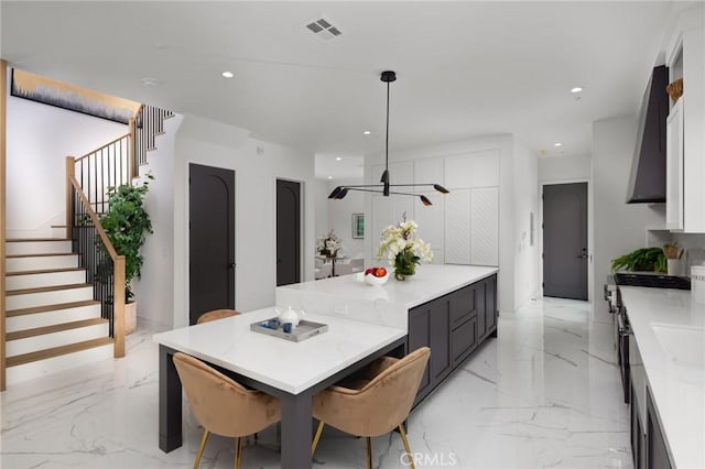 kitchen with white cabinetry, wall chimney range hood, hanging light fixtures, and light stone countertops