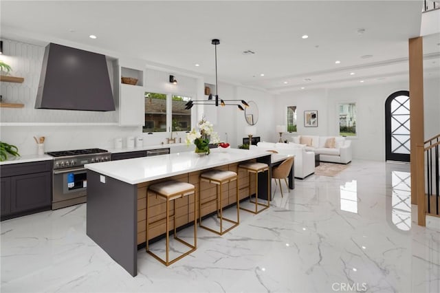 kitchen featuring pendant lighting, a kitchen island, wall chimney range hood, stainless steel stove, and a breakfast bar