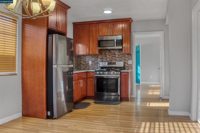 kitchen featuring light wood-type flooring, appliances with stainless steel finishes, tasteful backsplash, and a notable chandelier