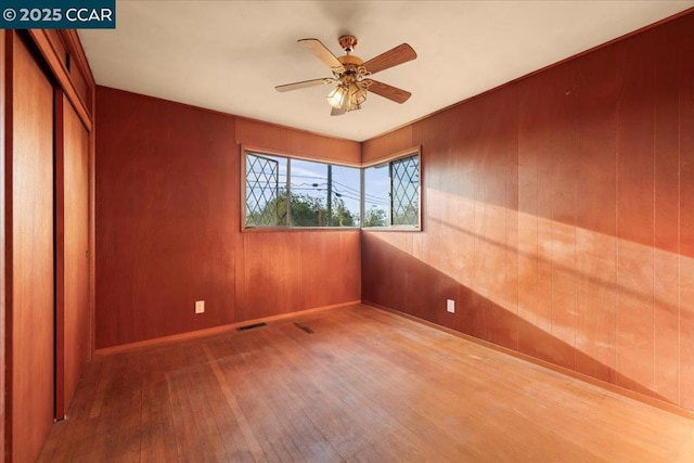 unfurnished room featuring ceiling fan, hardwood / wood-style floors, and wood walls