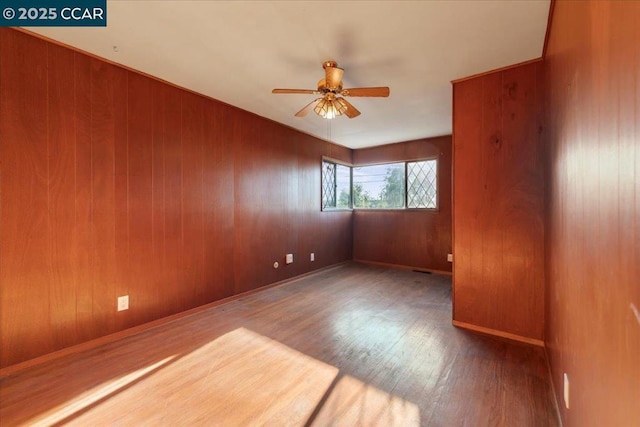 empty room with ceiling fan, wood-type flooring, and wooden walls