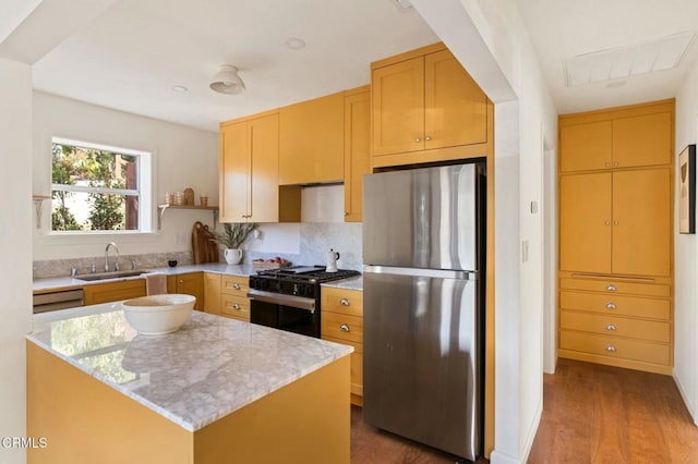 kitchen with wood-type flooring, stainless steel refrigerator, a kitchen island, black range with gas stovetop, and sink