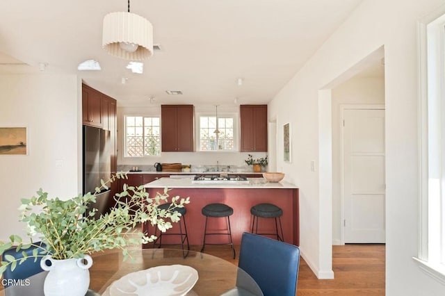 kitchen with pendant lighting, stainless steel fridge, kitchen peninsula, light wood-type flooring, and a breakfast bar area