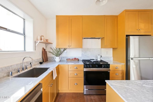 kitchen featuring light stone countertops, sink, stainless steel fridge, and gas range oven