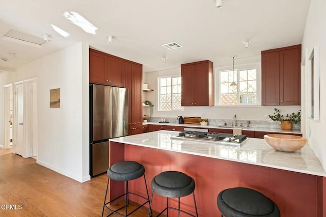 kitchen with appliances with stainless steel finishes, a kitchen bar, light hardwood / wood-style floors, sink, and light stone counters