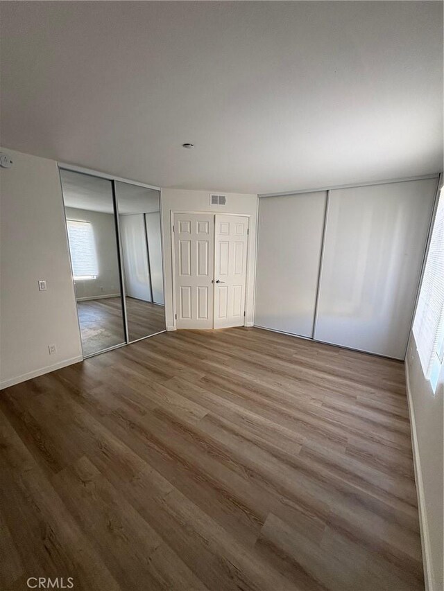 unfurnished bedroom featuring wood-type flooring, multiple closets, and multiple windows