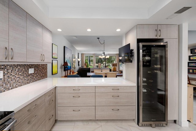 kitchen featuring tasteful backsplash, light brown cabinetry, wine cooler, kitchen peninsula, and a chandelier