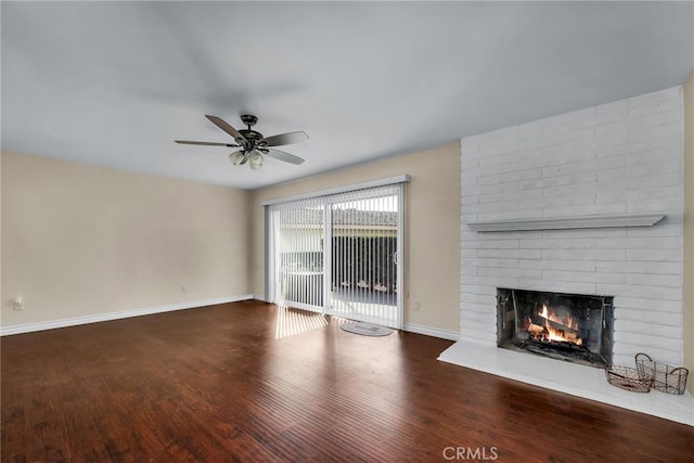 unfurnished living room with ceiling fan, a brick fireplace, and dark wood-type flooring