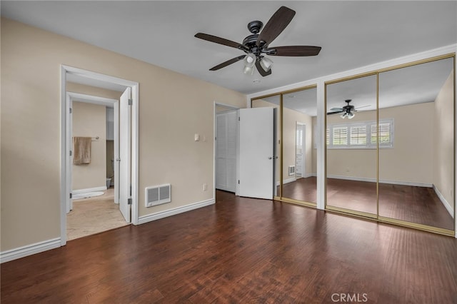 unfurnished bedroom featuring ceiling fan, multiple closets, ensuite bathroom, and wood-type flooring