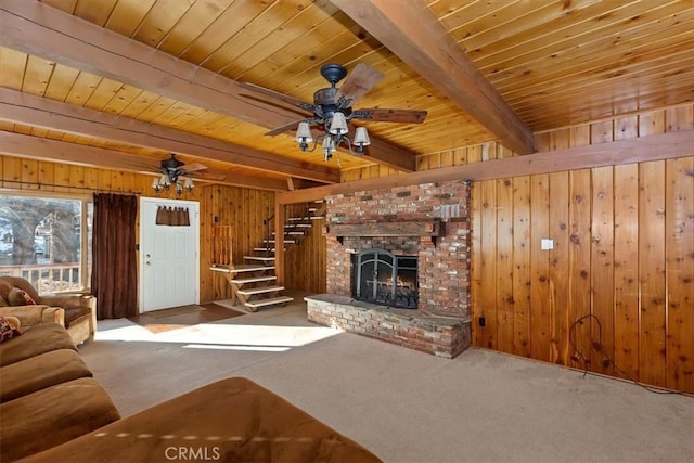 unfurnished living room featuring light carpet, a fireplace, wood walls, ceiling fan, and beam ceiling