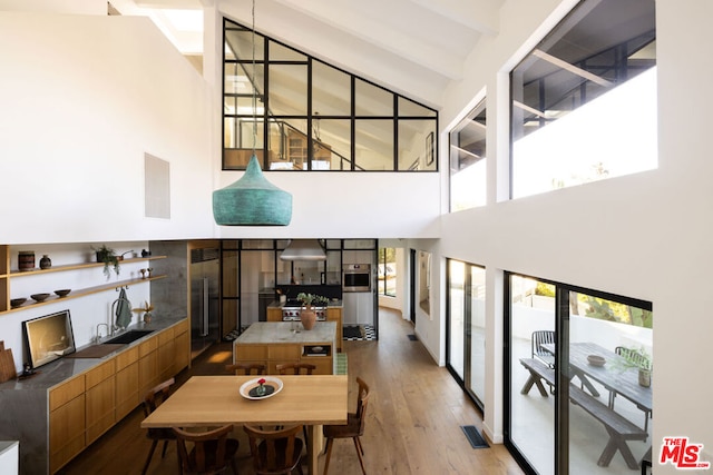 dining room featuring light wood-type flooring, a wealth of natural light, a high ceiling, and beamed ceiling