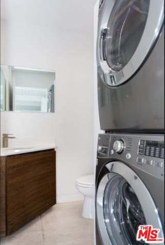 laundry area with stacked washer and dryer, light tile patterned floors, and sink