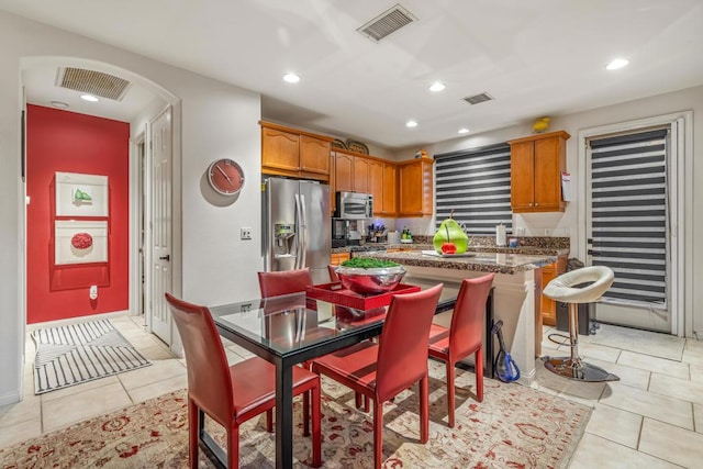 kitchen with a kitchen breakfast bar, appliances with stainless steel finishes, dark stone counters, light tile patterned flooring, and a center island