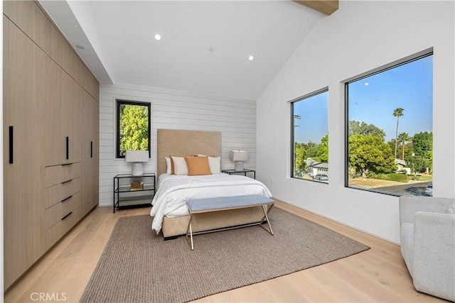 bedroom with high vaulted ceiling, beam ceiling, wooden walls, and light hardwood / wood-style floors