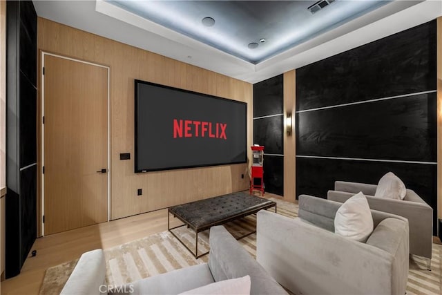 cinema featuring light hardwood / wood-style floors, a tray ceiling, and wooden walls