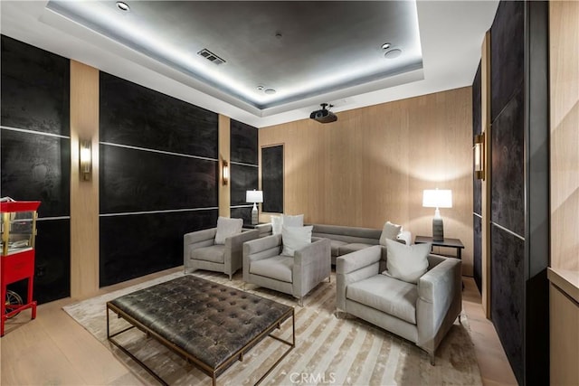 home theater room featuring wooden walls, light hardwood / wood-style floors, and a tray ceiling