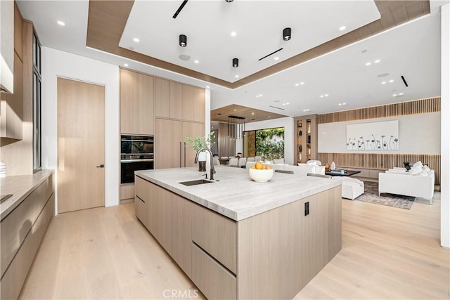 kitchen featuring a spacious island, light brown cabinets, sink, a tray ceiling, and light hardwood / wood-style flooring