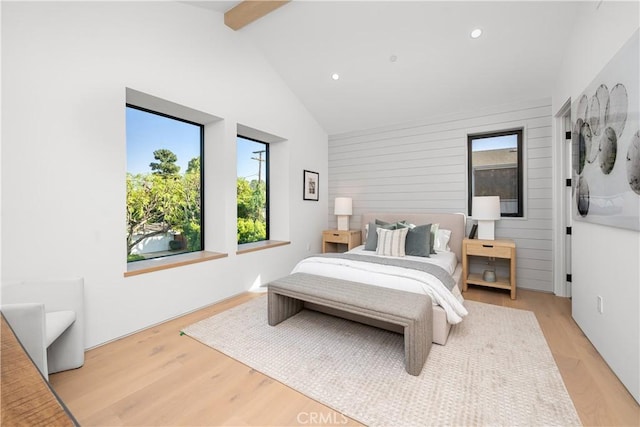 bedroom featuring beam ceiling, light hardwood / wood-style flooring, wooden walls, and high vaulted ceiling