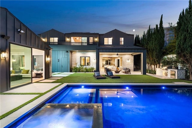 back house at dusk with an outdoor fire pit, a lawn, a patio area, exterior kitchen, and a balcony