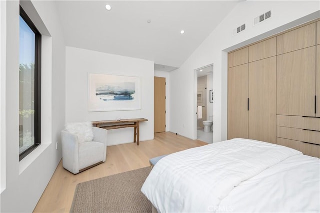 bedroom featuring vaulted ceiling, a closet, light hardwood / wood-style flooring, and ensuite bath