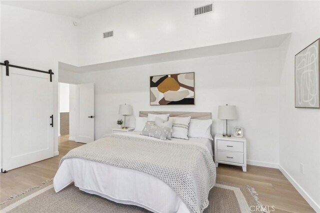 bedroom featuring light hardwood / wood-style floors, a towering ceiling, and a barn door