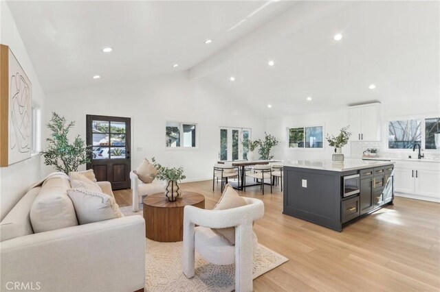 living room featuring high vaulted ceiling, sink, light hardwood / wood-style flooring, and beam ceiling