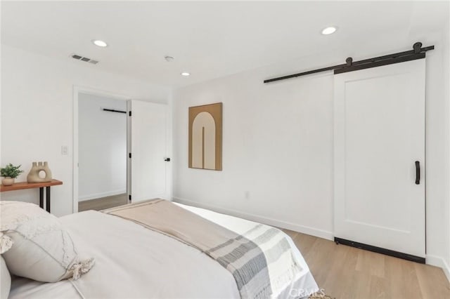 bedroom with a barn door and light wood-type flooring