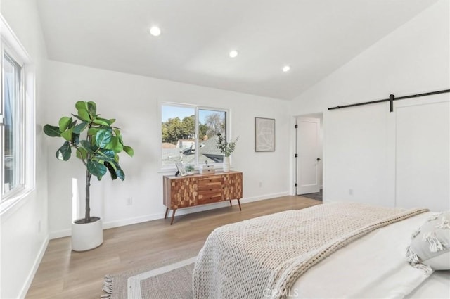 bedroom featuring lofted ceiling, light hardwood / wood-style flooring, and a barn door