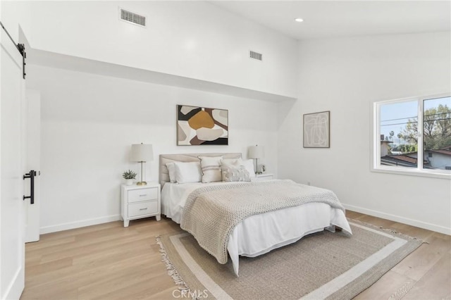 bedroom featuring high vaulted ceiling, light hardwood / wood-style floors, and a barn door