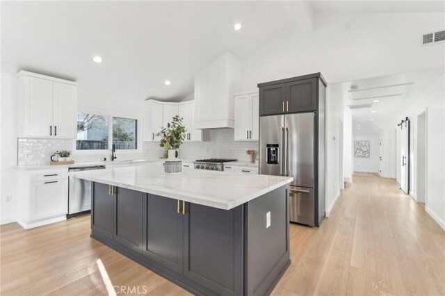 kitchen featuring appliances with stainless steel finishes, lofted ceiling with beams, white cabinetry, light stone counters, and a kitchen island