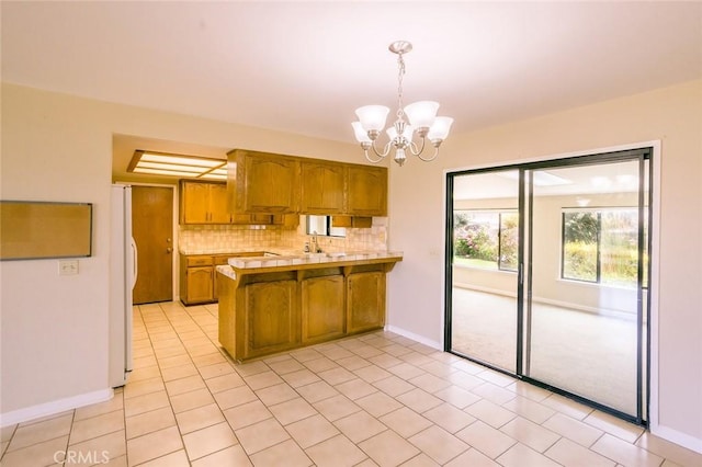 kitchen featuring white fridge, an inviting chandelier, kitchen peninsula, backsplash, and pendant lighting