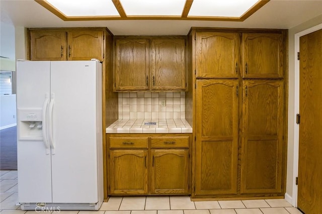 kitchen featuring white fridge with ice dispenser, light tile patterned floors, tile countertops, and tasteful backsplash