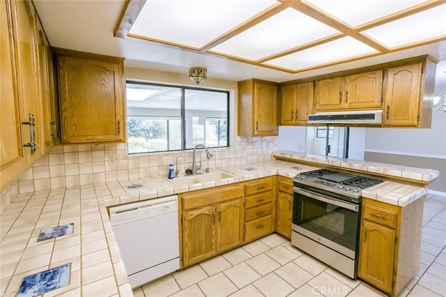 kitchen featuring tile countertops, kitchen peninsula, gas range, white dishwasher, and sink