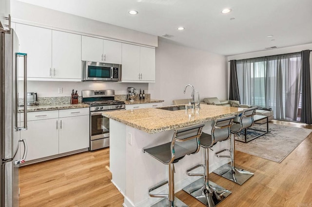 kitchen featuring white cabinetry, light hardwood / wood-style flooring, stainless steel appliances, and a center island with sink