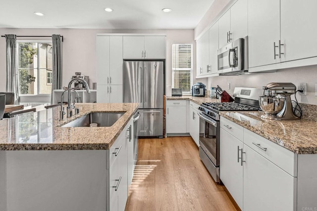 kitchen with sink, appliances with stainless steel finishes, white cabinetry, light stone countertops, and light hardwood / wood-style floors