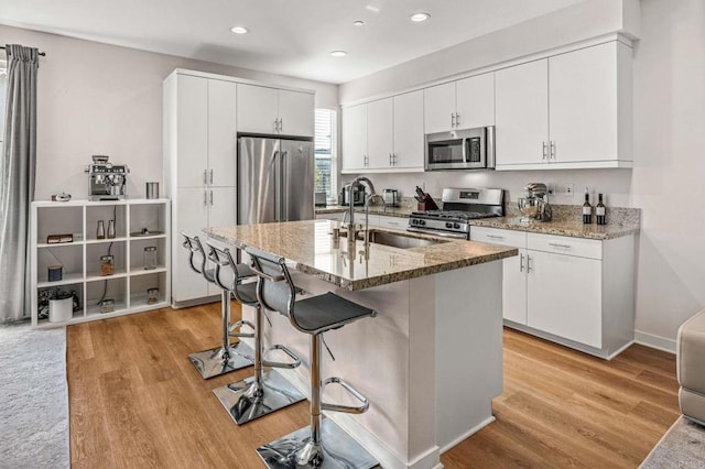 kitchen featuring sink, appliances with stainless steel finishes, a kitchen island with sink, light hardwood / wood-style floors, and white cabinets