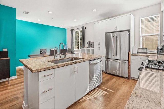 kitchen featuring sink, a center island with sink, light wood-type flooring, appliances with stainless steel finishes, and white cabinets