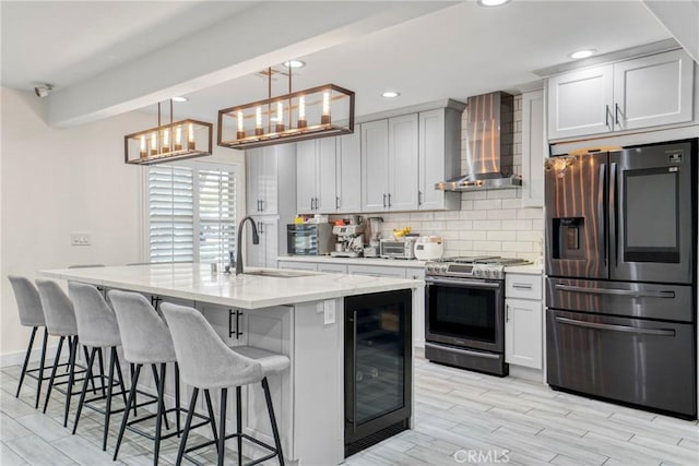 kitchen featuring wine cooler, hanging light fixtures, appliances with stainless steel finishes, an island with sink, and wall chimney exhaust hood