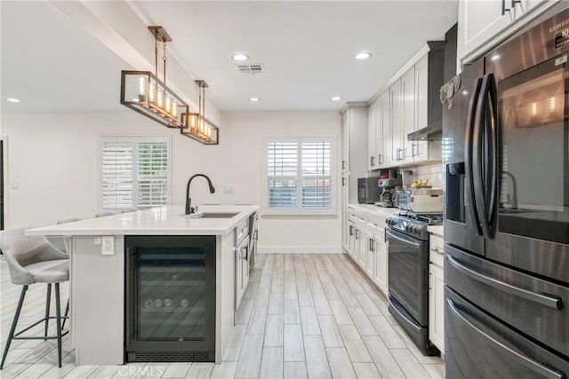 kitchen with a center island with sink, stainless steel refrigerator with ice dispenser, range with gas stovetop, hanging light fixtures, and beverage cooler