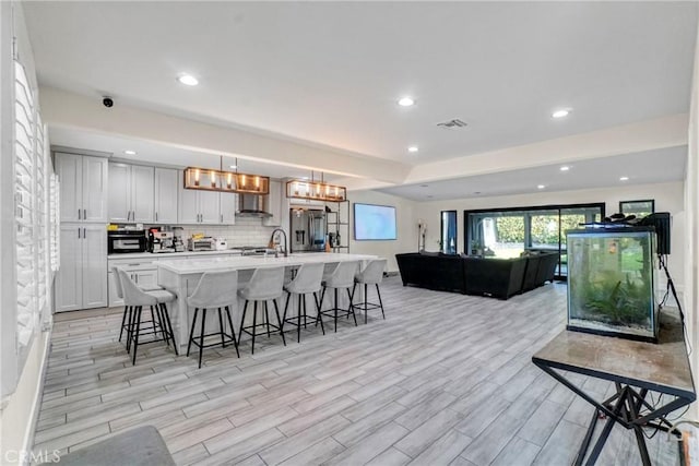 kitchen featuring decorative light fixtures, white cabinetry, an island with sink, a kitchen breakfast bar, and stainless steel fridge